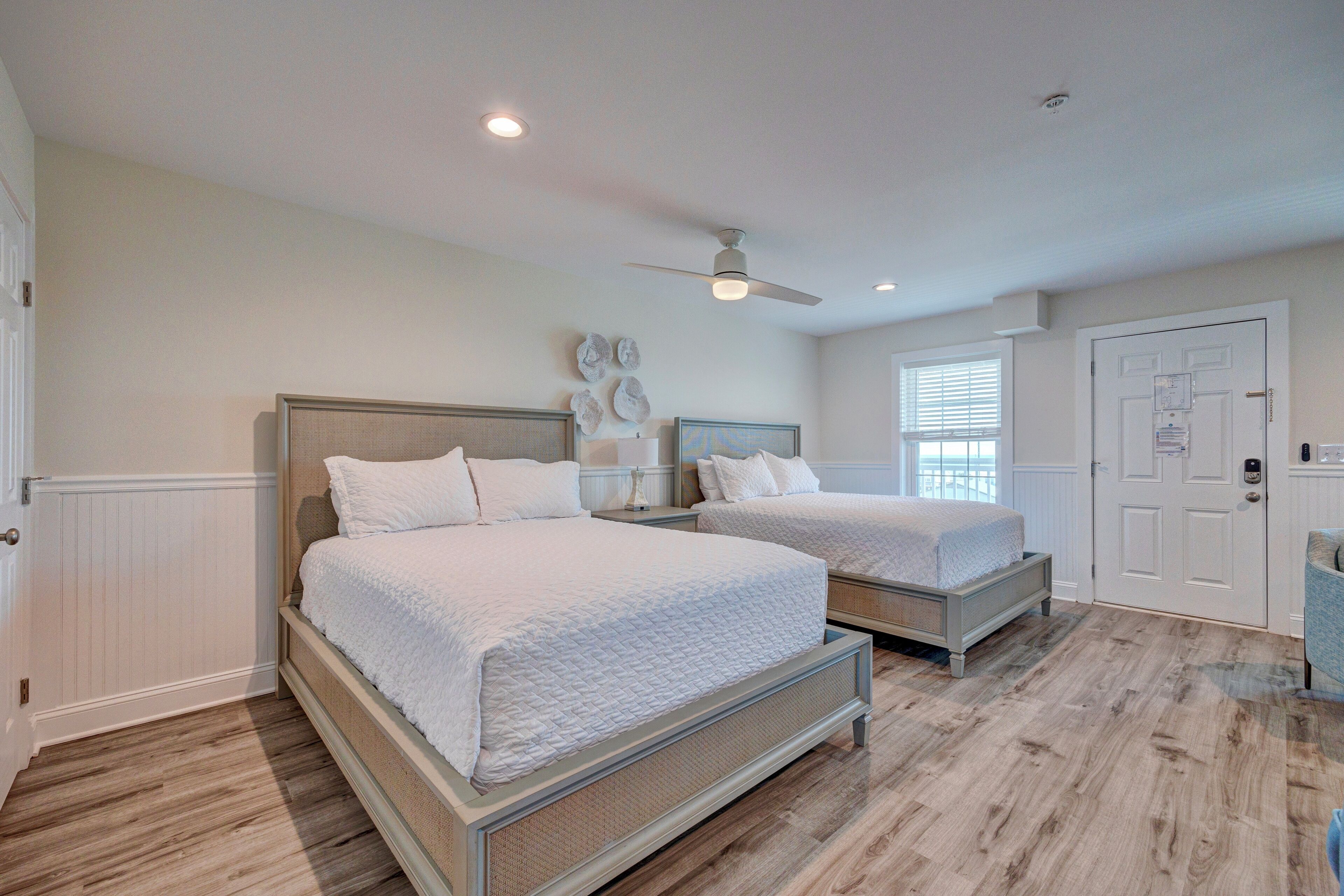 A bedroom with two beds, a ceiling fan, and a window with blinds.