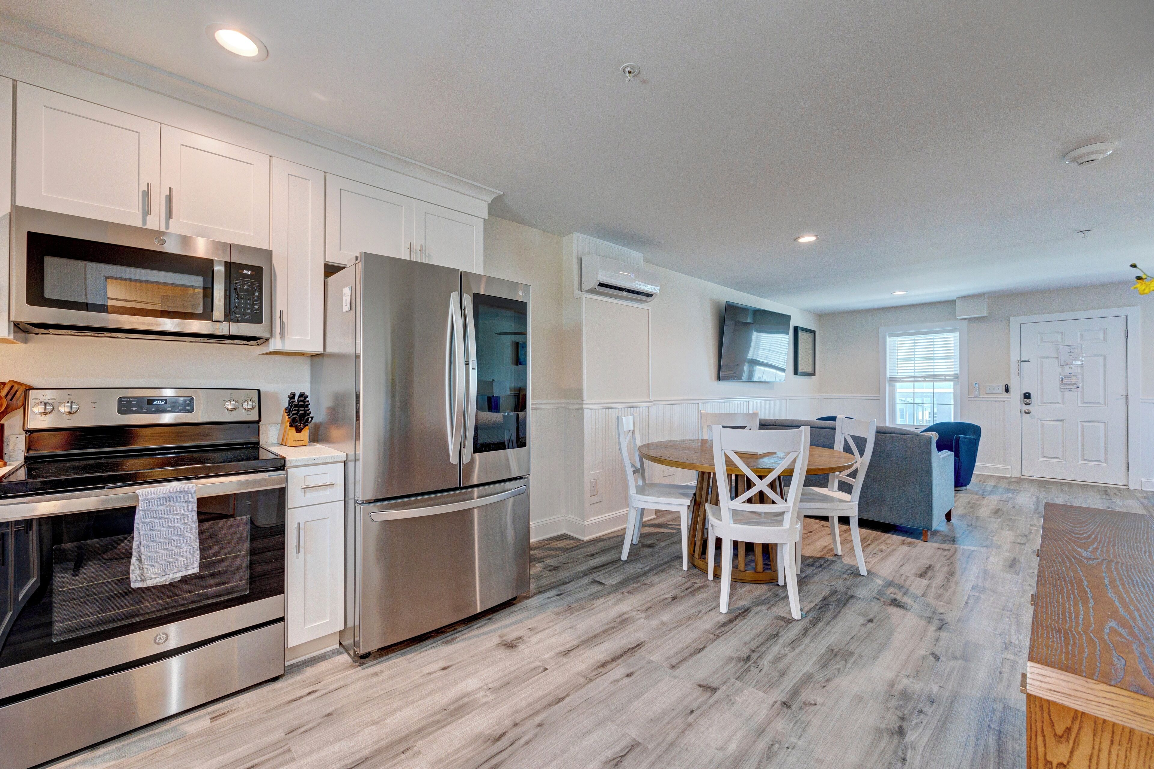 A modern kitchen with stainless steel appliances, white cabinetry, and a dining area with a wooden table and chairs.