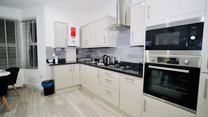 A modern kitchen with white cabinets, a black countertop, a built-in oven, and a gas stove. - ILford Station (Ilford)