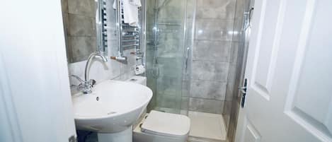 Un baño con lavamanos blanco, inodoro y zona de ducha con mampara de vidrio.