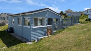 A small, single-story mobile home with a porch, a fenced yard, and a clear sky. - D37 Irene, Riviere Towans (Hayle)