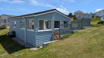A small, single-story mobile home with a porch, a fenced yard, and a clear sky.