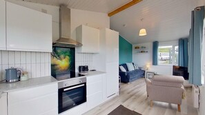 A modern kitchen with a built-in oven and a dining area with a sofa and a chair. - D37 Irene, Riviere Towans (Hayle)