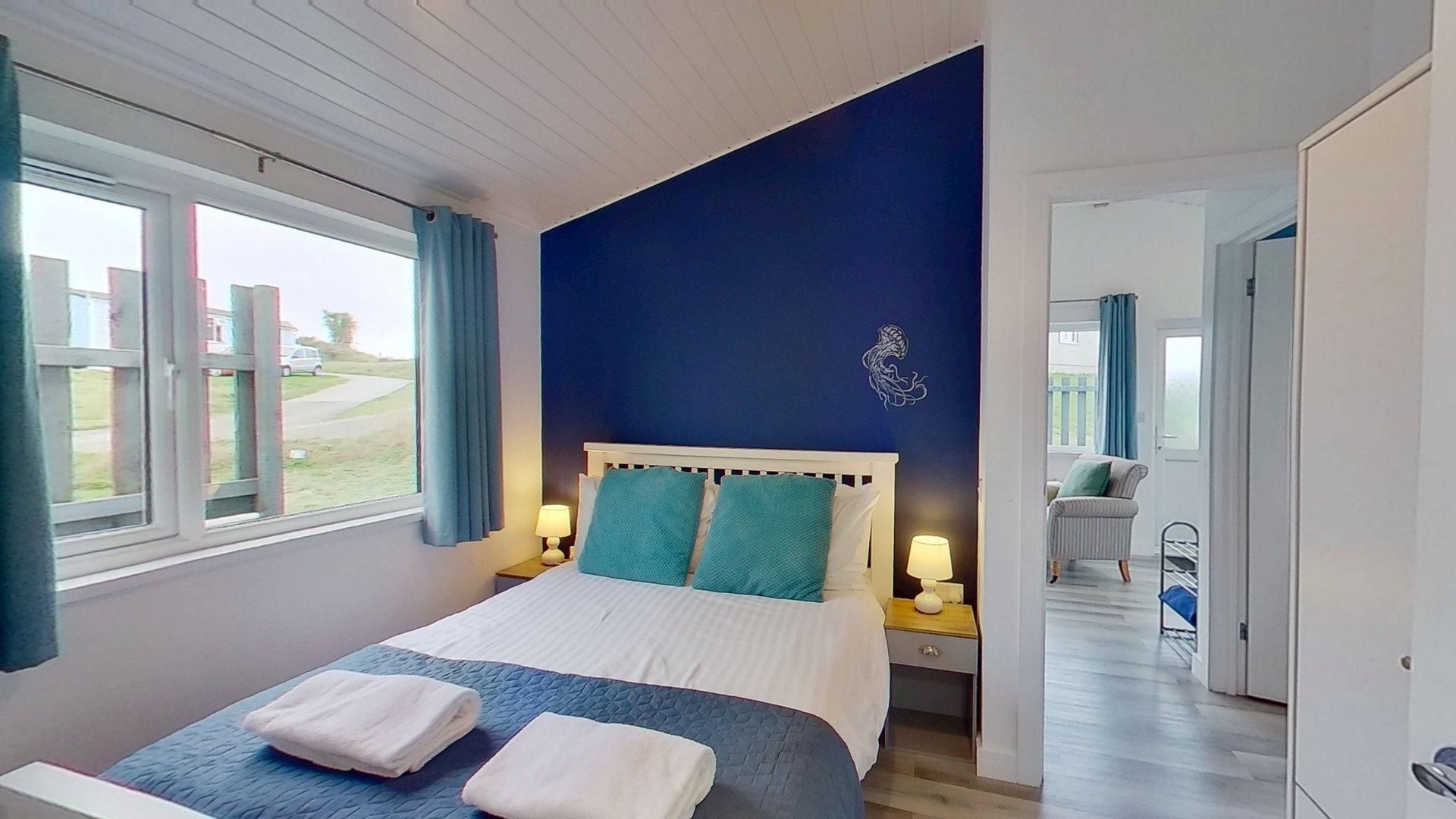 Une chambre à coucher avec un lit, deux tables de chevet, une fenêtre et une vue sur l’extérieur.