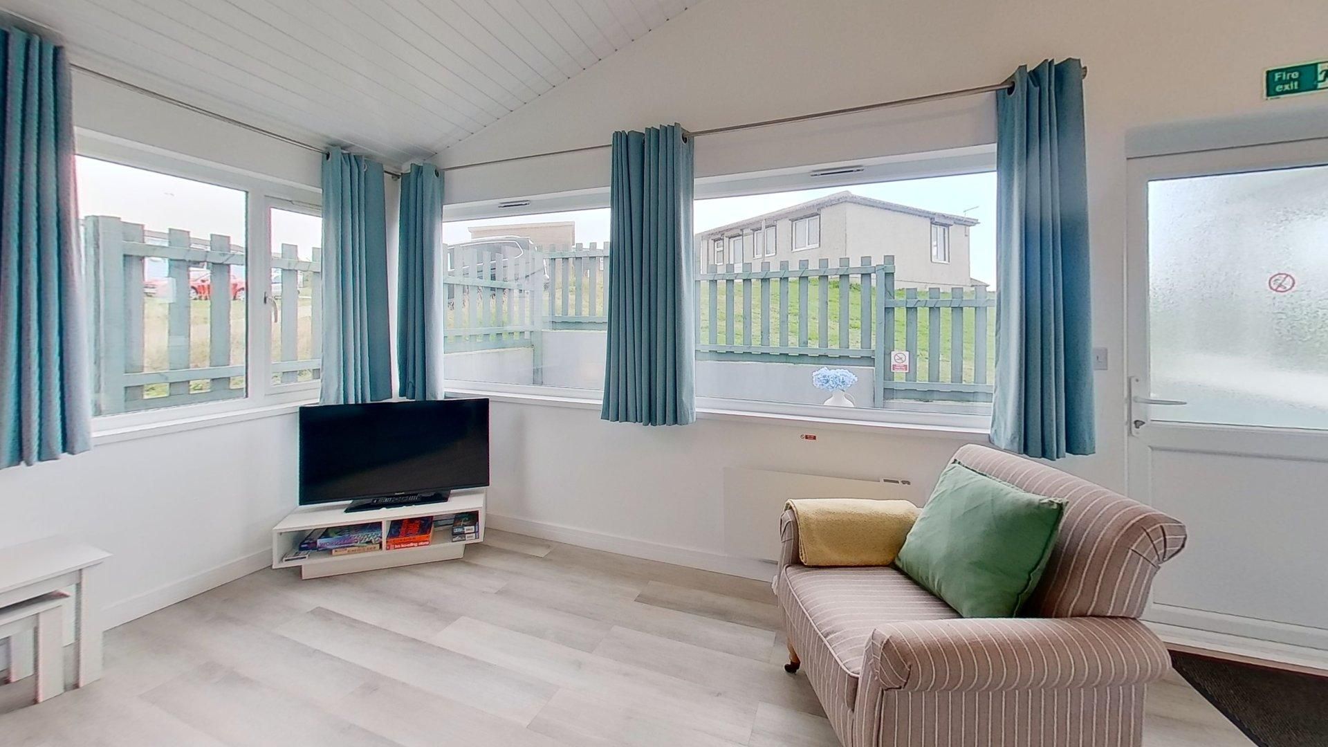 A room with a flat-screen TV on a stand, a striped sofa with cushions, and a window with curtains.