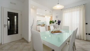 A dining area with a glass table, white chairs, and a pendant light. - Villa dido Nini (Žminj)