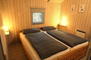 A room with a wooden paneled wall, a bed with a patterned bedspread, a window with a curtain, and wall-mounted lights.
