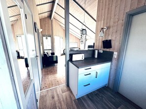 A modern kitchen with a built-in oven, a sink, and a countertop. There is a wooden ceiling and a view of a living area with a sofa.
