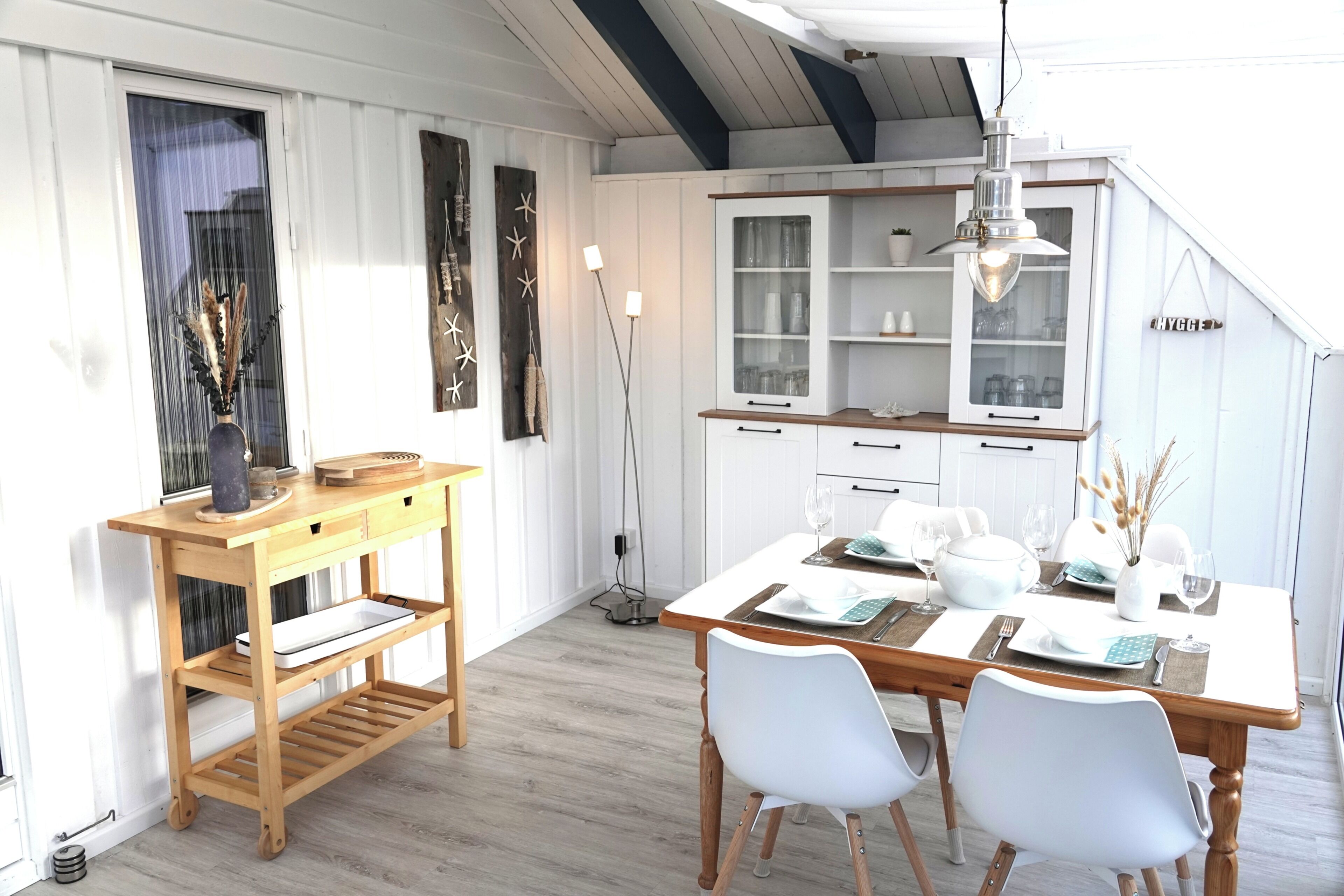 Een eethoek met een houten tafel, witte stoelen en een kast met glazen deuren.