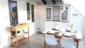 Zona pranzo con tavolo in legno, sedie bianche e pensile con ante in vetro.