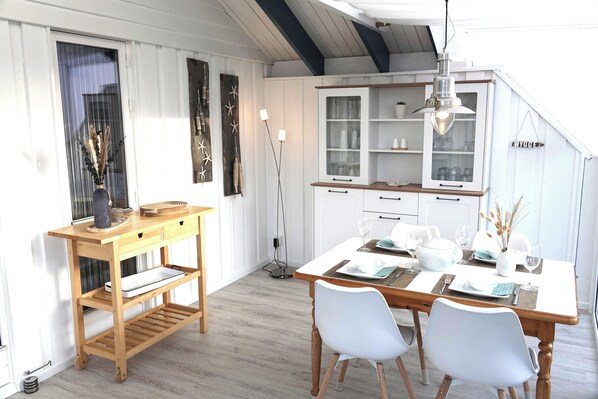 Un comedor con una mesa de madera, sillas blancas y un mueble con puertas de cristal.