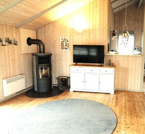 A cozy room with a wood stove, a flat-screen TV, a white cabinet, and a grey rug.