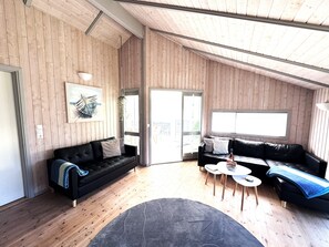 A modern interior with wooden walls, a black leather sofa, a small round table, and a large window.