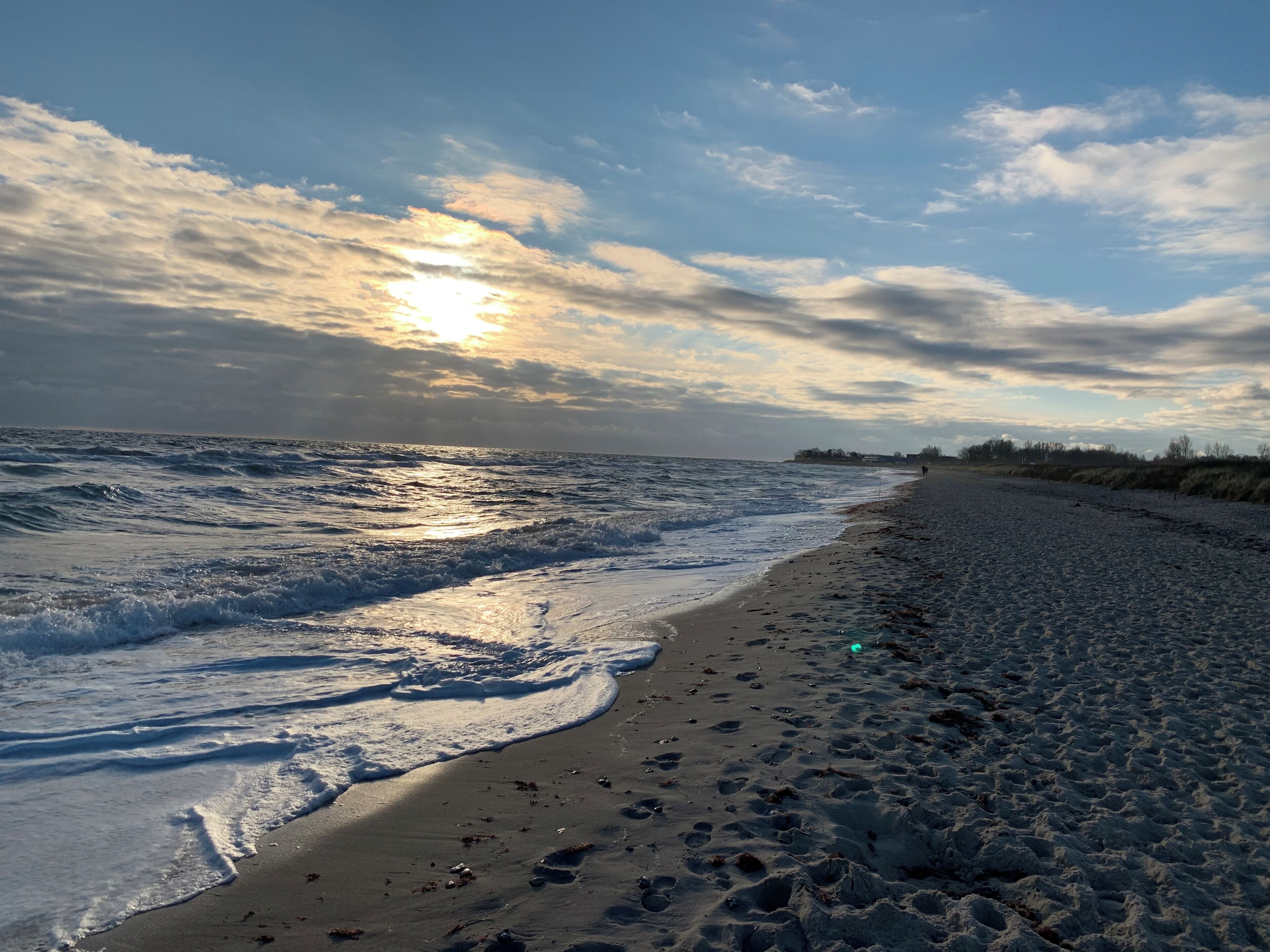 Een strand met golven, een heldere lucht en een verre kustlijn.