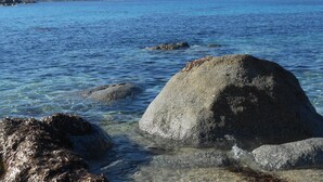 A coastal scene with clear water, large rocks, and distant hills. - BRAND-NEW SELF-CONTAINED STUDIO WITH GARDEN IN MARINE AREA (Corbara)