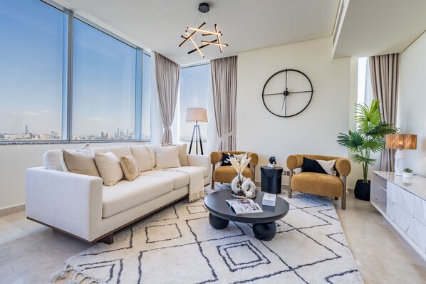 A modern living room with a sofa, armchair, coffee table, and a city view through large windows.