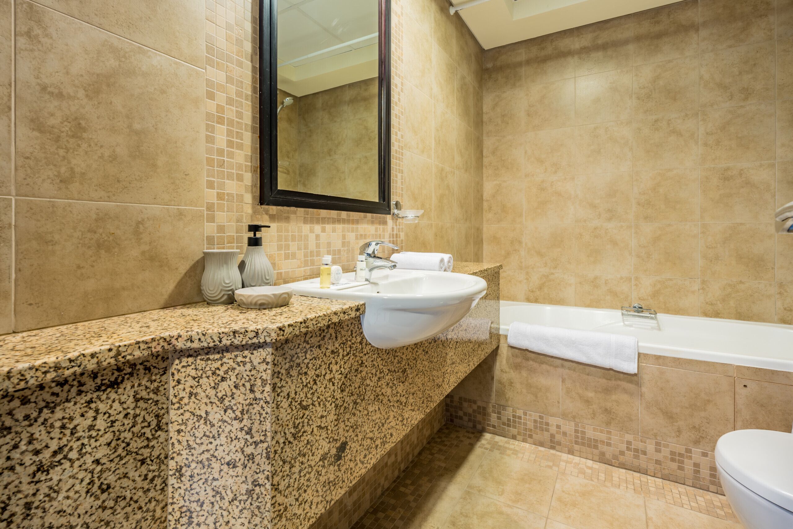 Une salle de bain avec un comptoir en granit, un lavabo blanc et une baignoire.