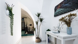 A hallway with white walls, a white table with decorative items, a potted plant, and a painting on the wall. - The Apple Duplex by Wonderful Italy (Catania)