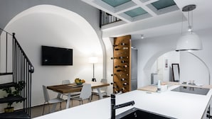 A modern kitchen with a central island, a dining area with a wooden table, and a staircase with black railings. - The Apple Duplex by Wonderful Italy (Catania)