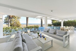 A modern outdoor lounge area with a sofa, coffee table, and dining set overlooking a beach.