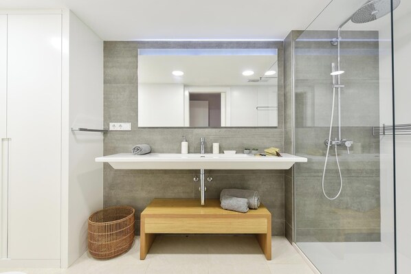Un baño moderno con un lavamanos, espejo y ducha blancos.