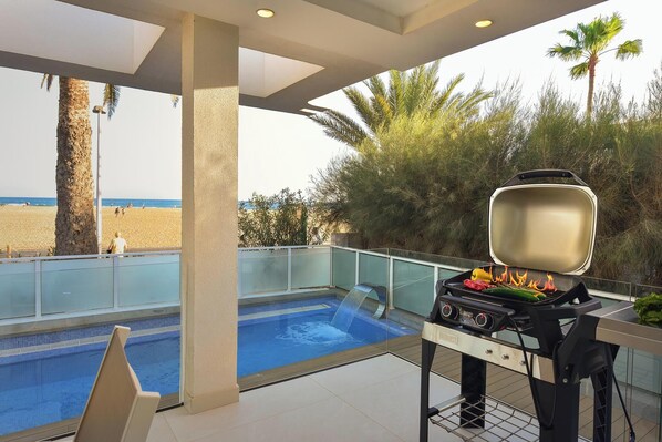 Un área junto a la piscina con una parrilla, vistas a la playa y una fuente de agua.