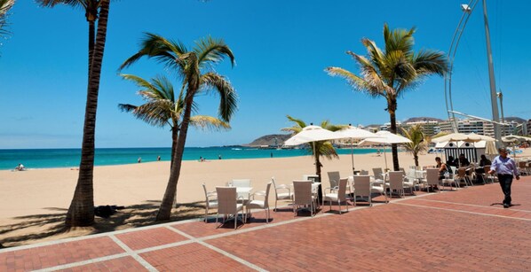A beachside patio with white chairs and umbrellas, palm trees, and a view of the beach and ocean. - Oasis Serenity by VillaGranCanaria (Maspalomas)