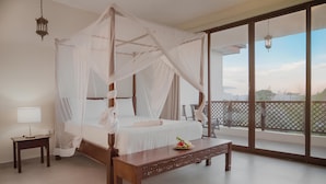 Una cama con dosel y cuatro postes, una mesita de noche de madera, una mesita auxiliar y vistas al balcón exterior.