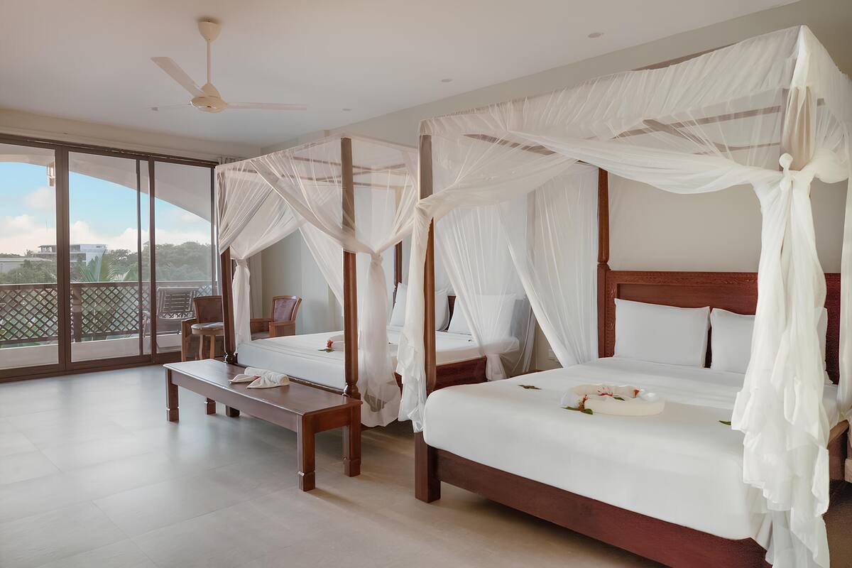 A bedroom with two beds, a ceiling fan, and a large window with a view of greenery.