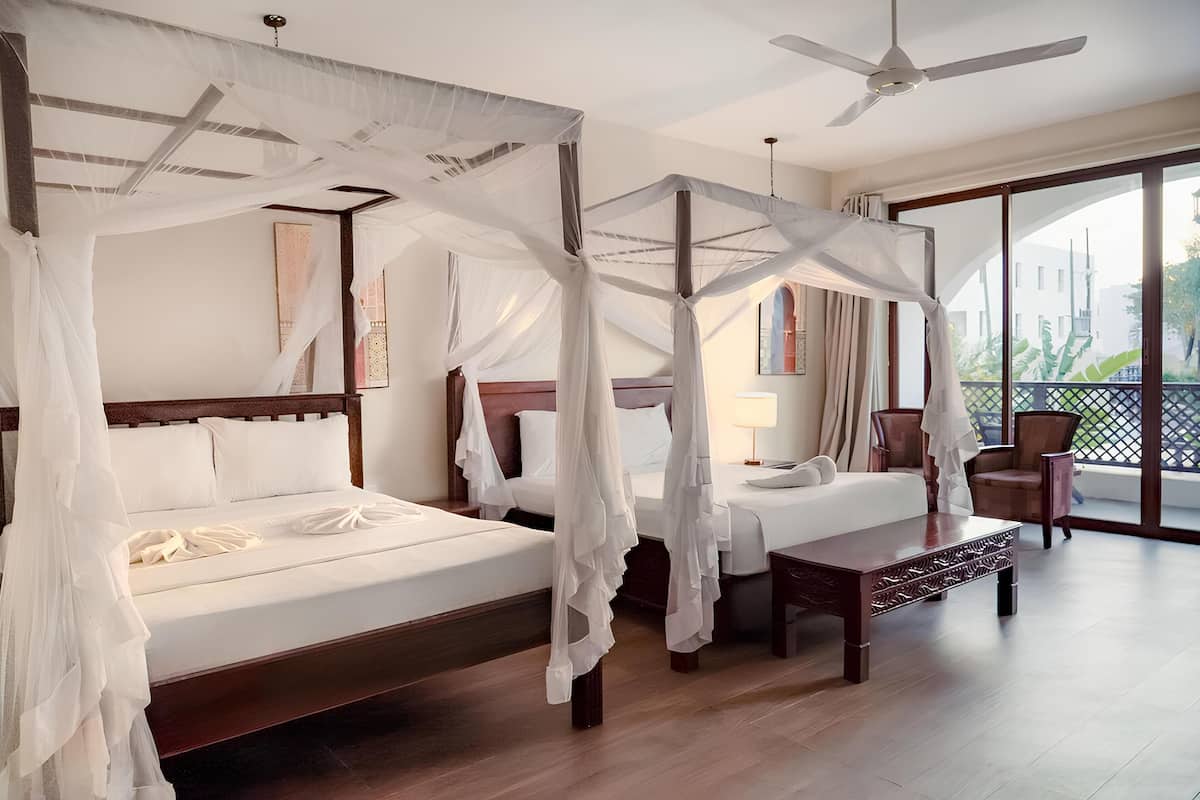 A bedroom with two beds, a ceiling fan, and a balcony with chairs.
