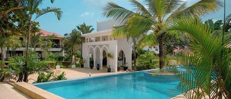 A swimming pool surrounded by palm trees and a building with arches.