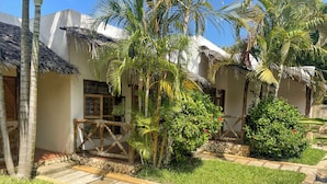 Un resort tropical con cabañas de techo de paja, palmeras y un sendero de piedra.