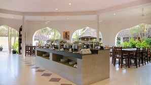 Amplio espacio interior con mesas de buffet, que incluye una isla central con recipientes de comida, rodeada de mesas y sillas de madera.