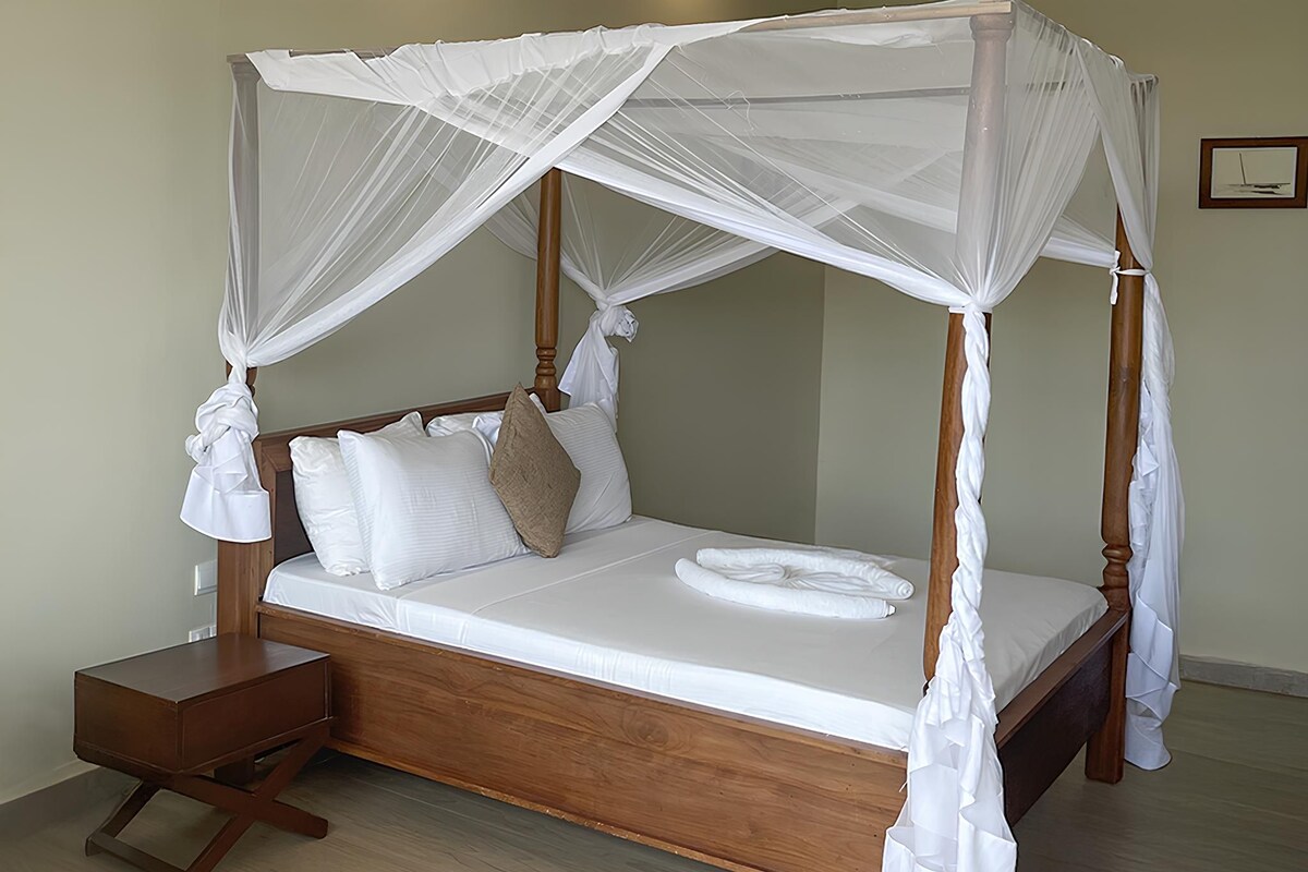 A four-poster canopy bed with white linens, a wooden headboard, and a bedside table.