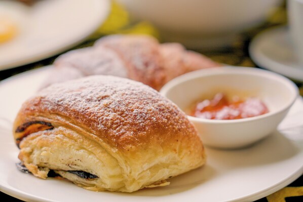 A pastry with powdered sugar on a plate, accompanied by a small bowl of jam.