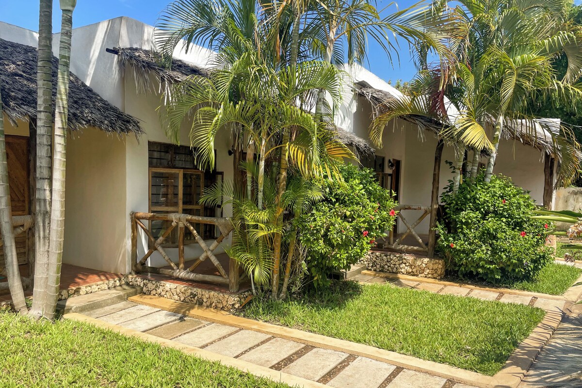 Un resort tropical con cabañas de techo de paja, palmeras y un sendero de piedra.