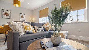 Un salon moderne avec un canapé gris, une plante en pot et une télécommande posée sur une table basse en bois.