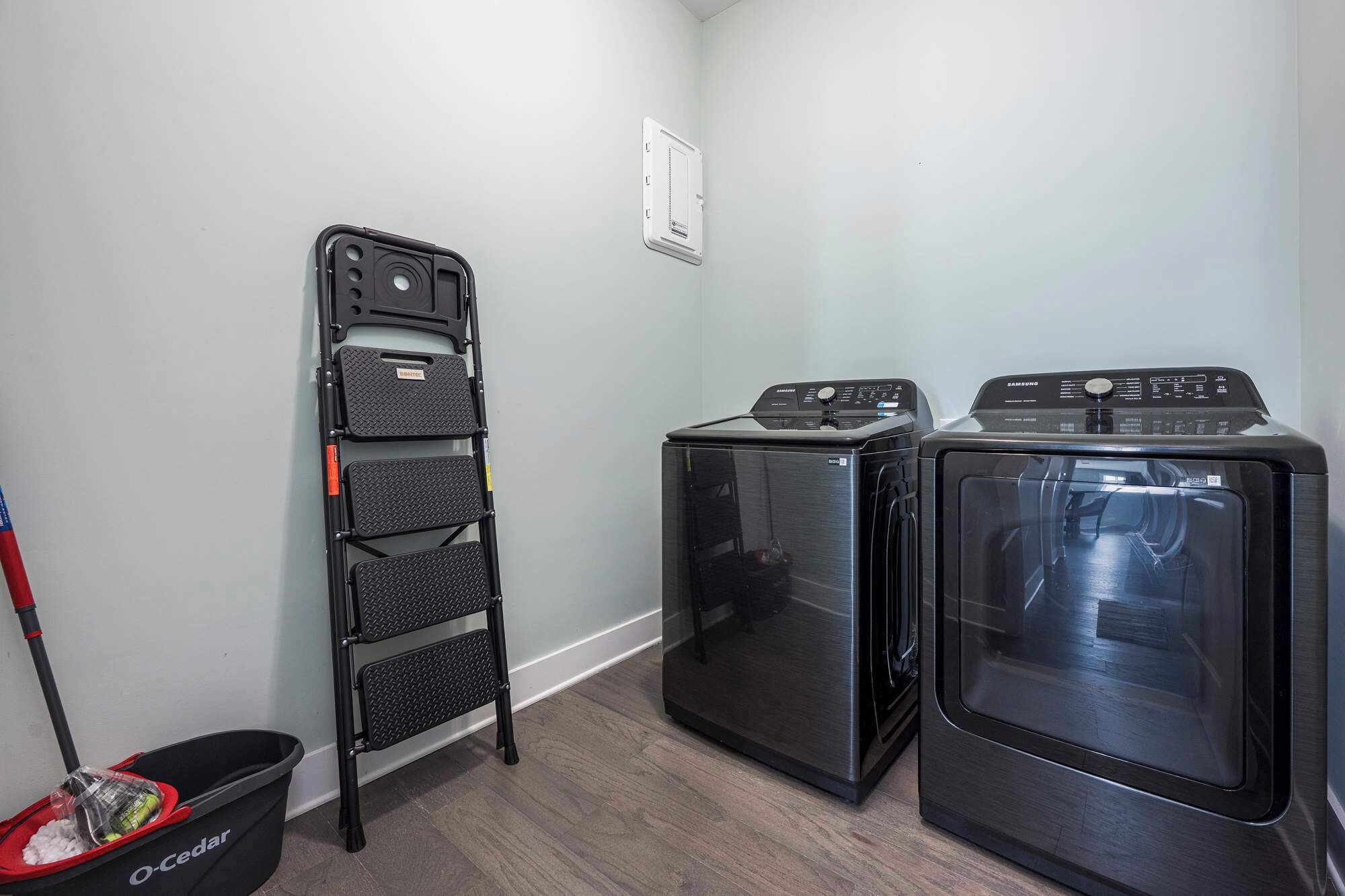 A laundry room with two stacked washer-dryers and a folding chair.