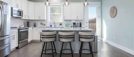 A modern kitchen with white cabinets, stainless steel appliances, and a central island with bar stools.