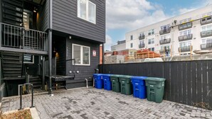 A building with a black exterior, a visible door, and a set of blue and green bins on the ground. - Modern Capitol Hill Apartment – 3 Min Walk to Metro! (Washington)