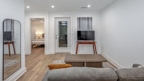 A modern living room with a flat-screen TV on a wooden stand, a sofa, a coffee table, and a mirror. - Modern Capitol Hill Apartment – 3 Min Walk to Metro! (Washington)