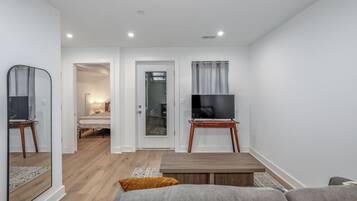 A modern living room with a flat-screen TV on a wooden stand, a sofa, a coffee table, and a mirror.