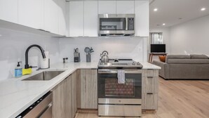 A modern kitchen with white cabinetry, a stainless steel microwave, a sink, and an oven. - Modern Capitol Hill Apartment – 3 Min Walk to Metro! (Washington)