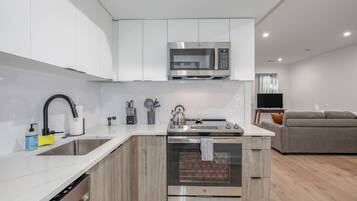 A modern kitchen with white cabinetry, a stainless steel microwave, a sink, and an oven.