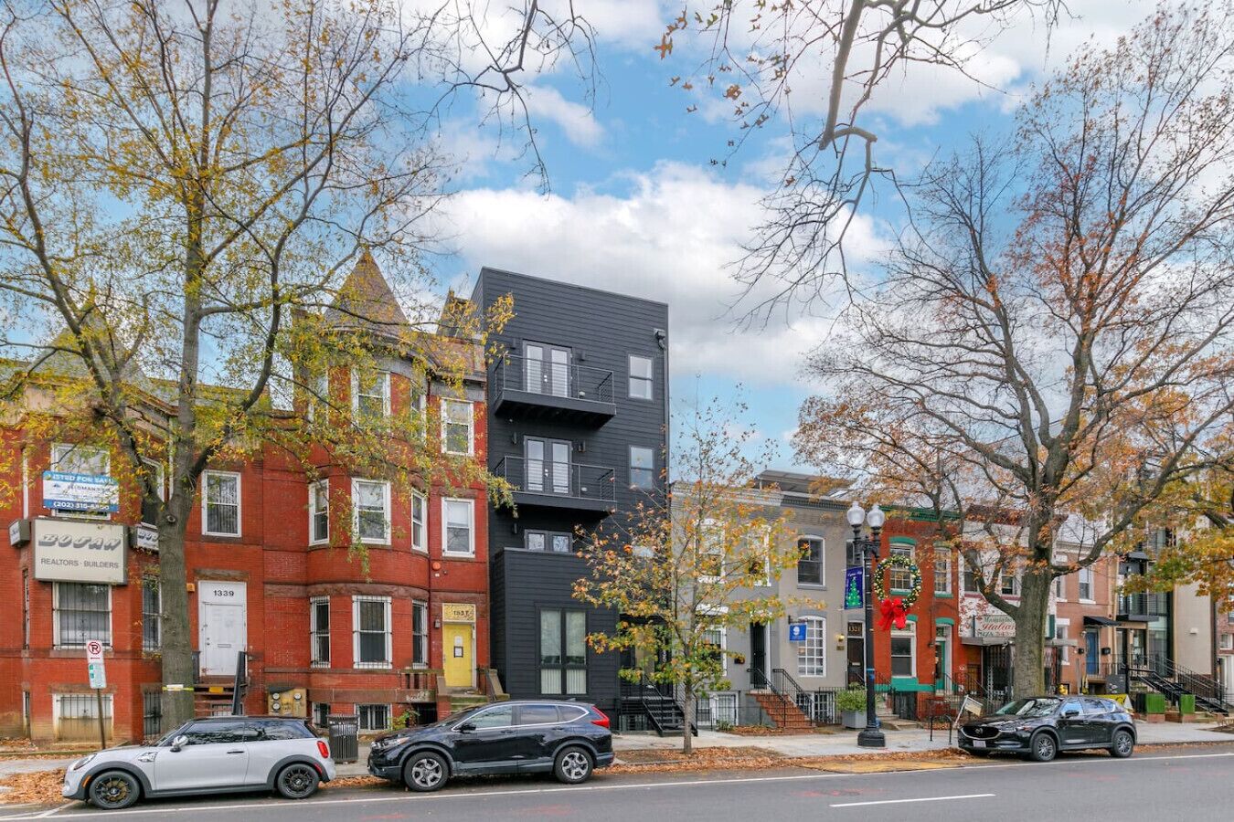 Una hilera de edificios de varios pisos con una mezcla de estilos arquitectónicos, incluyendo un edificio moderno de color negro y fachadas tradicionales de ladrillo rojo.