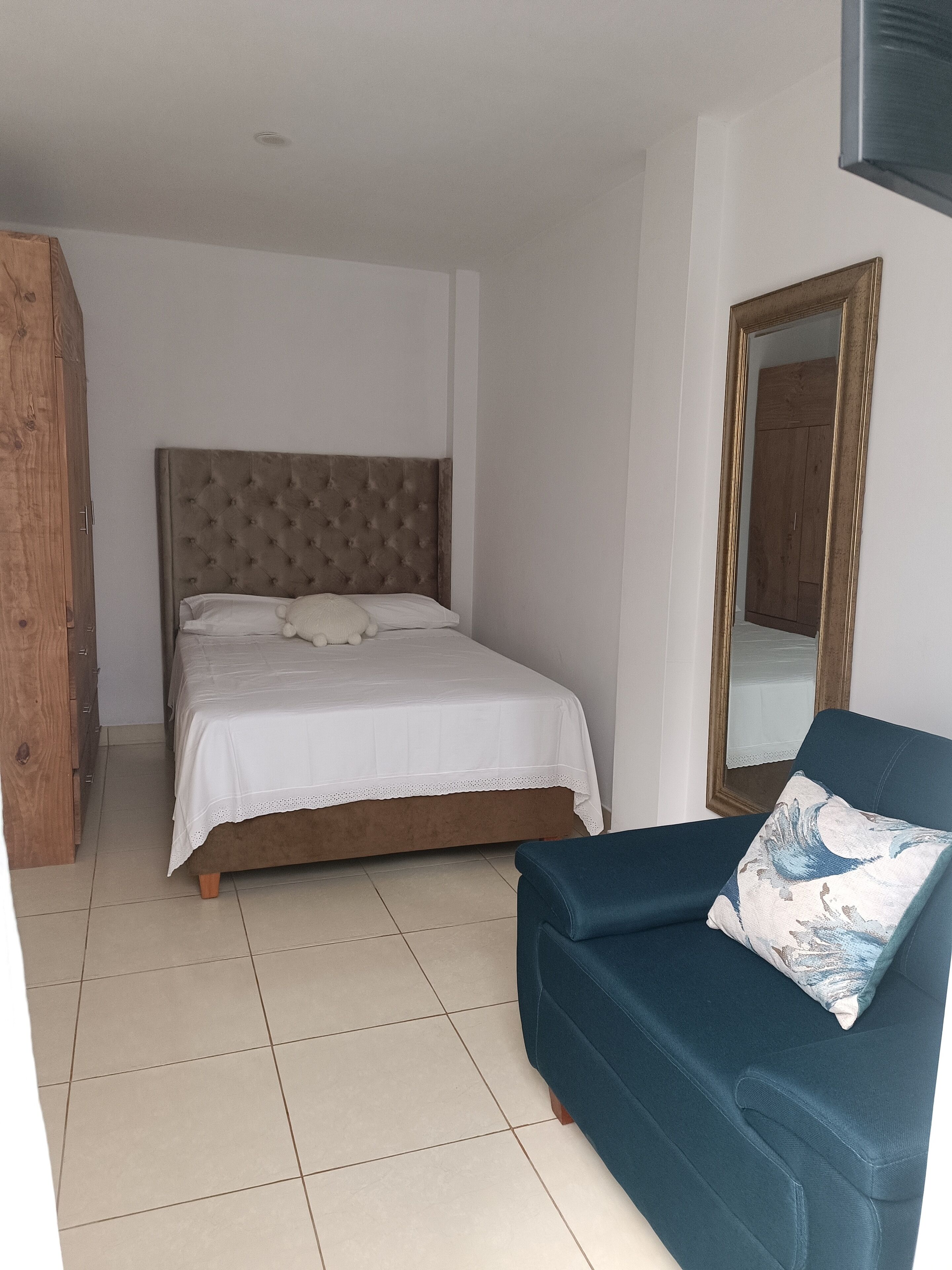Une chambre à coucher avec un lit, un canapé bleu, une armoire en bois et un miroir au mur.
