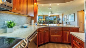 A modern kitchen with wooden cabinets, a large island, stainless steel appliances, and a view to the living area.