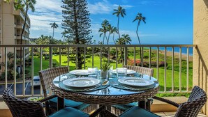 A round table set for four with wicker chairs, overlooking a landscaped garden and ocean view.