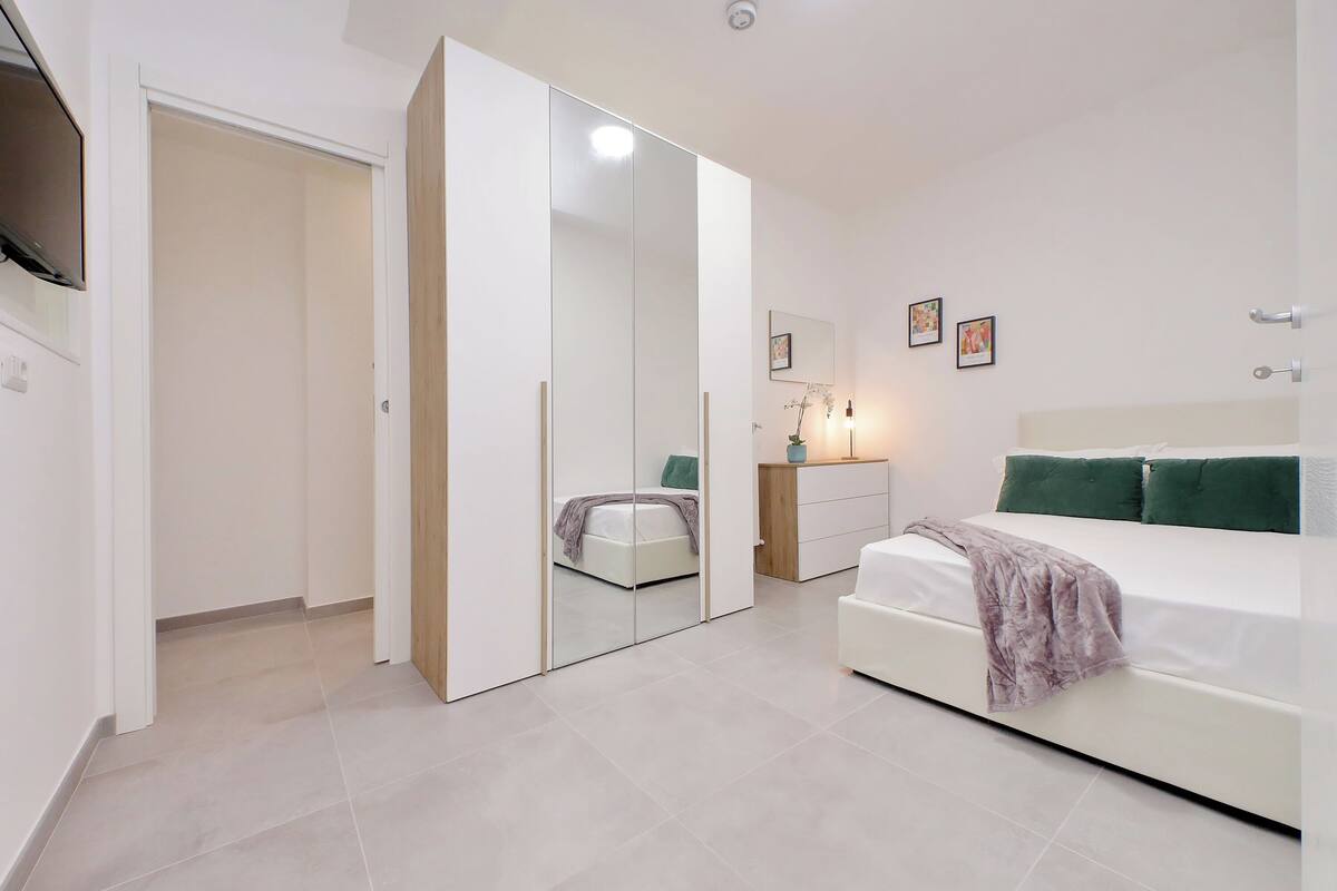 A modern bedroom with a bed, a wardrobe, a bedside table, and a mirror.