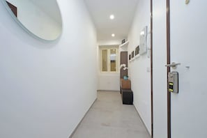 A narrow hallway with a round mirror on the left, a door with a security keypad on the right, and a small plant on a shelf. - YCH Bagnera Suites (Rome)